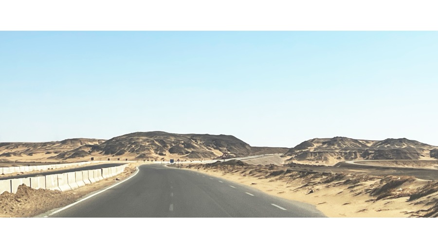 公路蜿蜒穿過沙漠，兩旁盡是起伏的沙丘與漫天黃塵